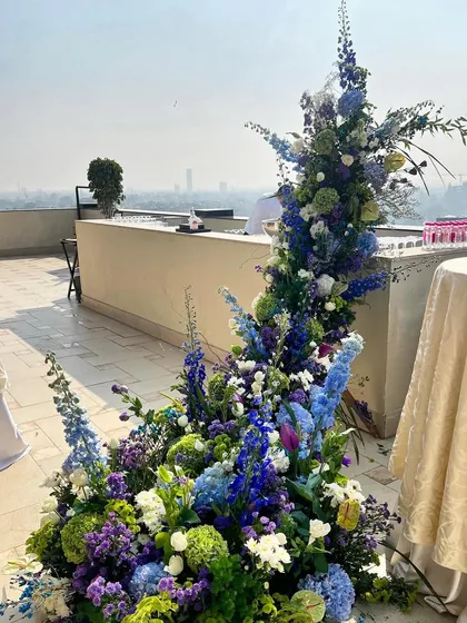 This cascading installation on a rooftop terrace was designed to feel like a waterfall of flowers. The blend of blues and greens against the city skyline creates a stunning contrast, proving that bold floral art can thrive in any environment.