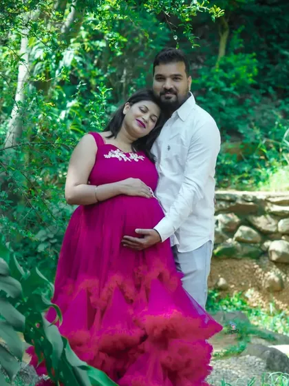 A peaceful moment between a couple in a green, wooded area. The way they hold each other and the baby bump conveys a sense of serenity and deep connection.