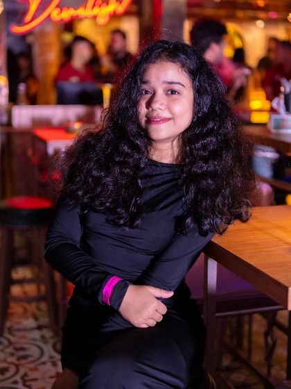 A guest smiling at her table, with the 'Devilish' neon sign in the background.