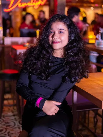 A guest smiling at her table, with the 'Devilish' neon sign in the background.