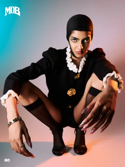 From a 'Neo-Baroque Noir' editorial, this shot combines modern attitude with classic elements. The model's crouched pose brings attention to the hand and wrist accessories, while the unique lighting creates a colorful gradient in the background.