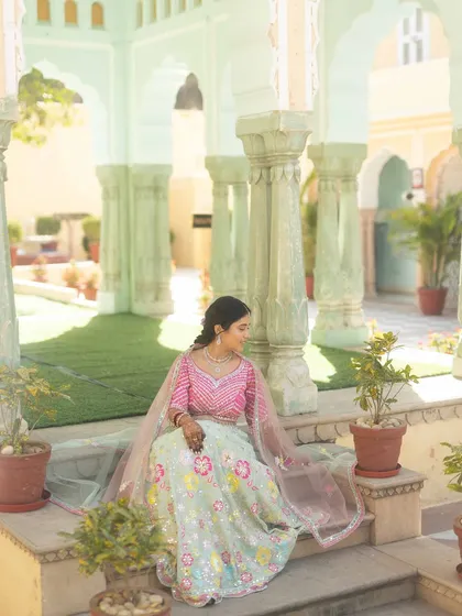 The bride, looking serene in her pastel lehenga, sits amidst the historic mint-green pillars of Chomu Palace. We help select locations within the venue for stunning portraits.