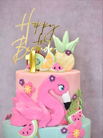 A close-up of the top tier of the flamingo cake, highlighting the number 1 candle, the gold "Happy Birthday" topper, and the detailed fondant pineapple and citrus slices.