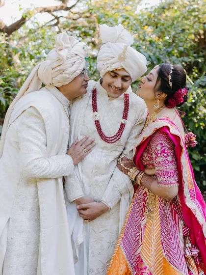 A sweet and candid moment between the groom and his parents, as his mother gives him an affectionate kiss on the cheek.