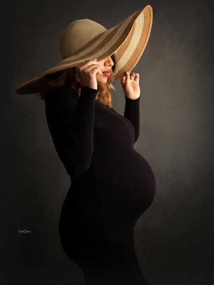Adding a stylish accessory like this wide-brimmed hat brings a touch of glamour to a classic black dress maternity portrait.