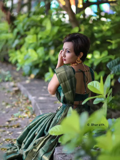 A candid, over-the-shoulder shot of the model in the green saree. The natural, leafy background complements the color of the outfit beautifully.