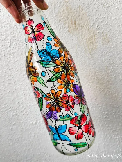 I love giving old bottles a new life with paint. This one is covered in a vibrant garden of flowers and butterflies, hand-painted directly onto the glass. It's a perfect example of how I can turn everyday objects into unique decor pieces.