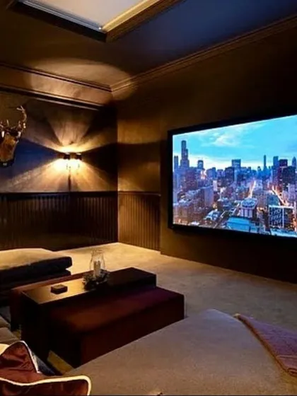 This design demonstrates a more relaxed and versatile media room concept, featuring a large, comfortable daybed and ottoman setup instead of traditional recliners. The warm, moody lighting and expansive screen create a cozy yet luxurious space for family movie nights.