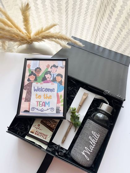 A modern and personalized onboarding kit. This hamper includes a custom-named bottle, a framed "Welcome to the Team" illustration, and other thoughtful items to welcome a new employee.