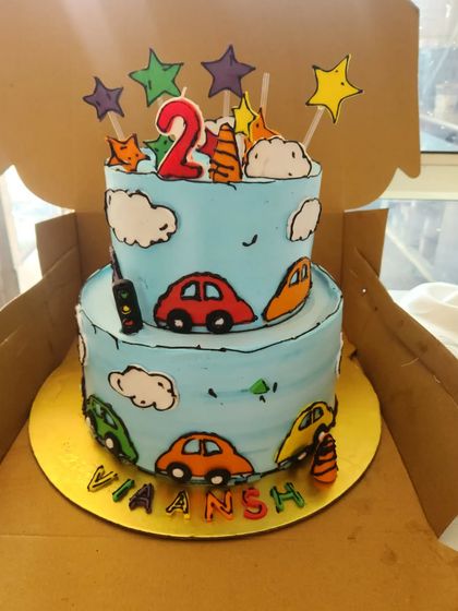A trendy comic book style cake. This two-tier cake is designed to look like a cartoon drawing, with bold black outlines on the cars and clouds, creating a unique and eye-catching effect.