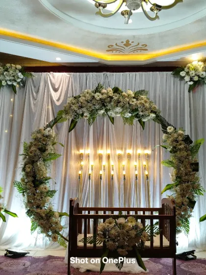An elegant naming ceremony setup with a circular arch of white flowers and greenery. The traditional wooden cradle is placed in the center, with soft candle lighting in the background to create a warm and inviting atmosphere.