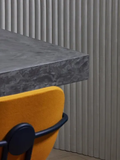 A corner detail of a grey, vertically ribbed 3D wallcovering against a dark stone countertop. The image highlights the clean lines and architectural quality of this modern, velvety design.