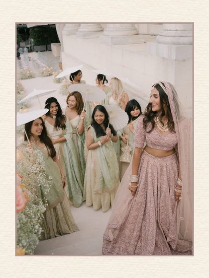 A framed portrait of the bride walking down the stairs, surrounded by her smiling bridesmaids holding umbrellas. The composition and soft colors give it a classic, painted feel.