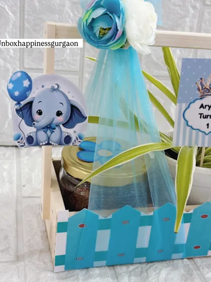 A close-up of the cute elephant sticker and personalized "Aryan Turns 1" tag on the blue-themed first birthday favor.