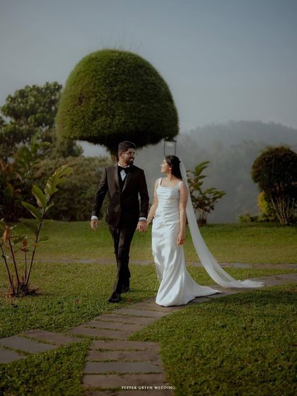 A classic walking portrait of the bride and groom in a beautifully manicured garden, her long veil trailing behind them.