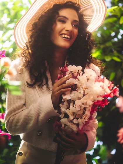 A joyful, light-filled portrait. The combination of a sun hat, a bouquet of flowers, and bright, airy lighting creates a feeling of happiness and natural beauty.