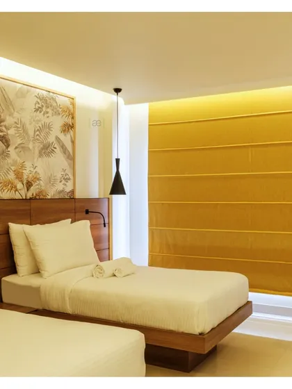 The twin bed configuration in another room, showing how the tropical-inspired wallpaper and warm yellow tones create a cohesive design language throughout the hotel.