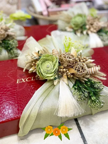 A beautifully wrapped gift box in red, adorned with a handcrafted bouquet of green and gold. This is a perfect example of how I handle individual gift wrapping with a luxurious touch.
