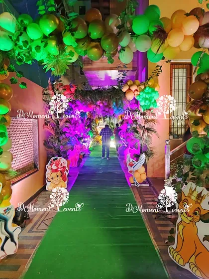 A view down the jungle-themed entrance tunnel, with a green carpet, dense balloon and foliage ceiling, and character cutouts lining the path.