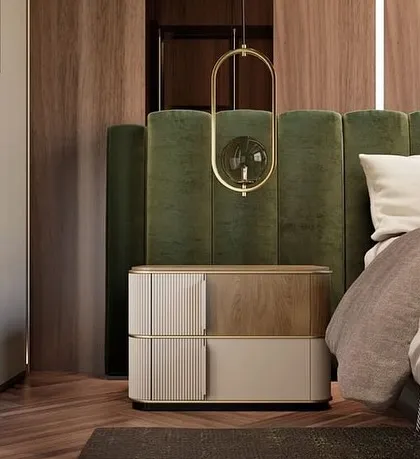 A bedside table combining veneer detailing with a painted finish, set against a deep green velvet headboard. The piece is elevated by stainless steel feet and handles in a polished gold finish.