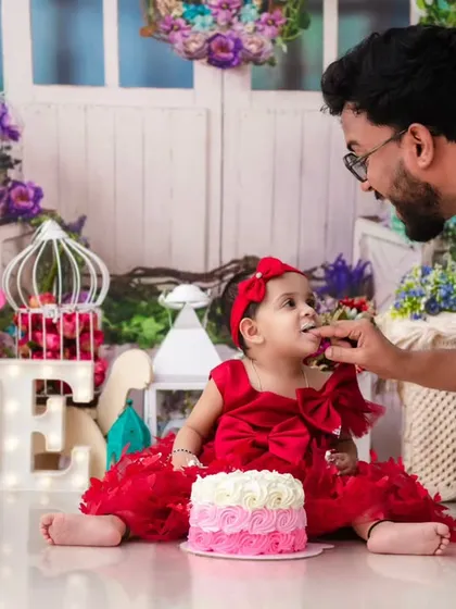 A father feeding his daughter her first birthday cake. Including parents in the cake smash creates beautiful moments of connection and shared joy.