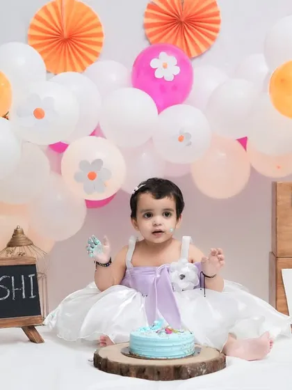 A sweet and messy moment from a second birthday cake smash. The pastel balloon backdrop and personalized chalkboard make the scene extra special.