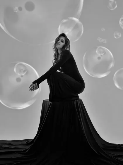 A dreamy and surreal black and white portrait. The addition of projected bubbles and the model's elegant pose create a whimsical and artistic fashion image.