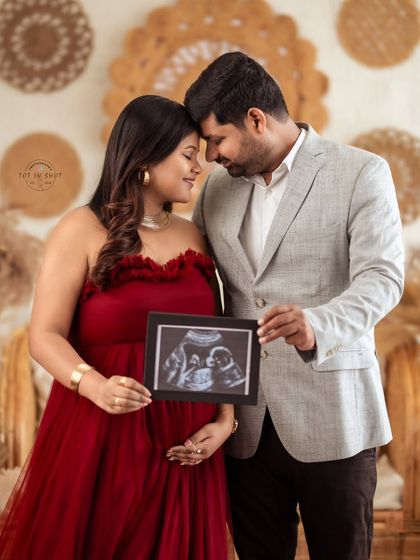 A beautiful couple's portrait, holding their baby's first picture. The mom-to-be is stunning in a vibrant red tulle gown.