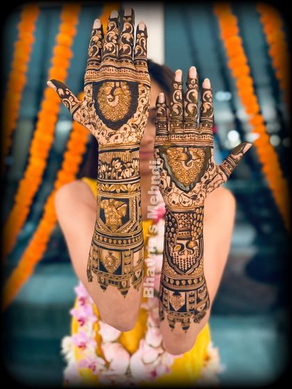 A classic bridal pose, with the hands held up to showcase the full, intricate design. This mehndi features shields with peacocks and elephants, along with bands of traditional patterns.