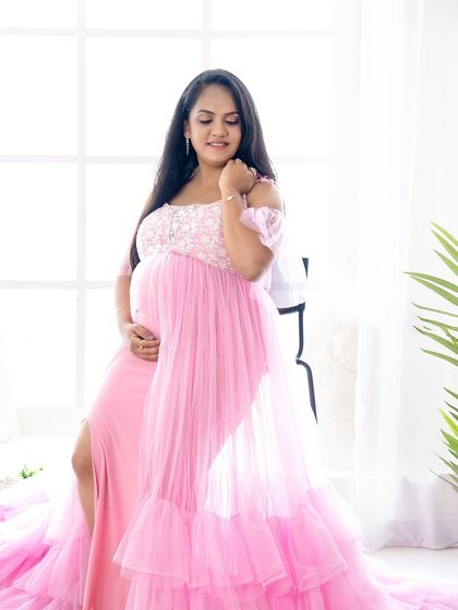 A soft and feminine portrait of a mom-to-be in a light pink gown, seated by a window with beautiful natural light.