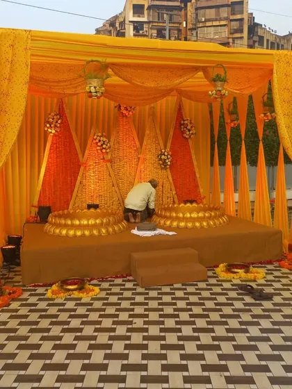This is a full Haldi stage setup with a backdrop of woven marigold cones and traditional urlis for the ceremony, all tied together with beautiful orange and yellow drapes.