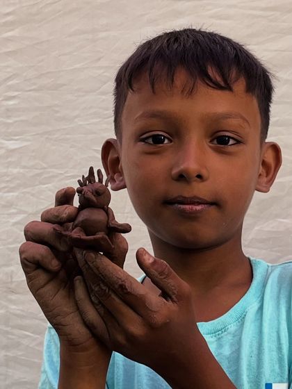 A young boy proudly presents his imaginative clay creature. Our community workshops are designed to be accessible and fun for everyone, regardless of age or experience.