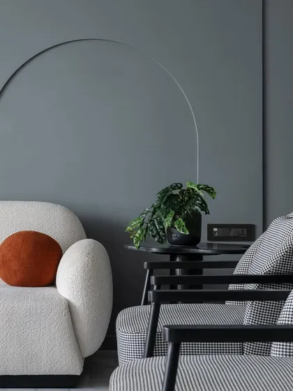 A detail shot from 'The House of Arcs', where a curved white sofa is paired with houndstooth-patterned armchairs, all set against a wall with subtle arched grooves.