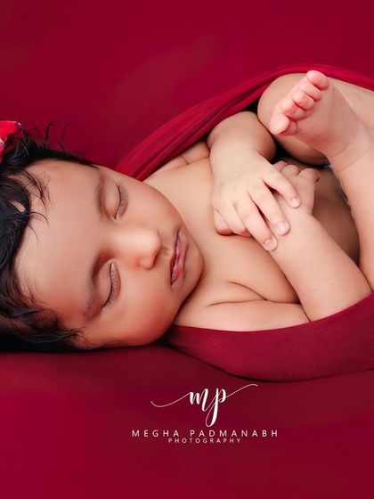 Another angle of the tucked-in pose, showcasing the baby's profile and the gentle curve of their back. The simple red backdrop makes the portrait pop.