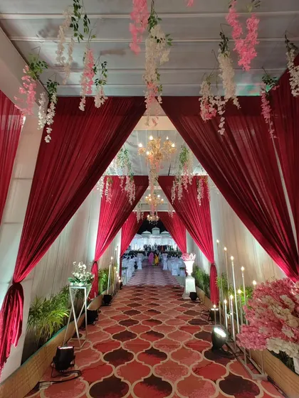 A clear, straight-on view of the red and white draped corridor. The symmetry of the drapes, chandeliers, and lighting creates a formal and grand path leading to the wedding festivities.