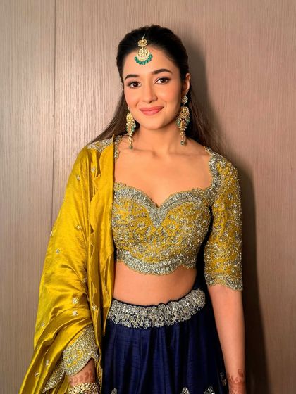 The full haldi look, featuring a stunning yellow and blue lehenga. The makeup is kept subtle and glowing to complement the vibrant outfit.