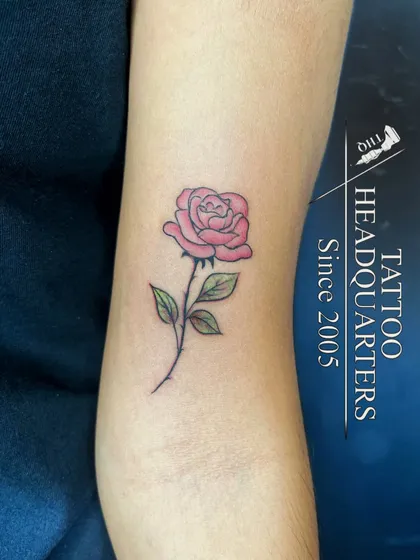 A beautiful, soft pink rose tattoo with green leaves, showcasing our skill with color and delicate designs.