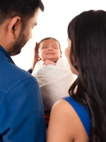 That first sleepy smile is pure magic. This intimate shot captures a newborn's joyful expression as his parents gaze down at him, their faces framing the beautiful moment.