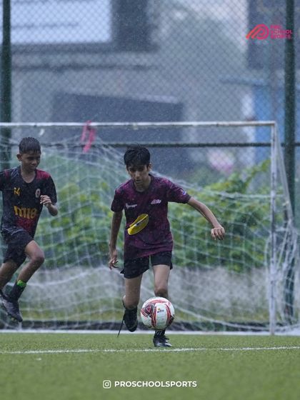Playing through the rain, our player stays focused on controlling the ball near the goal.