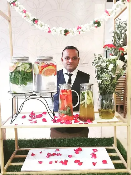 A member of my team standing behind a rustic wooden cart serving different kinds of detox water, ready to welcome guests.