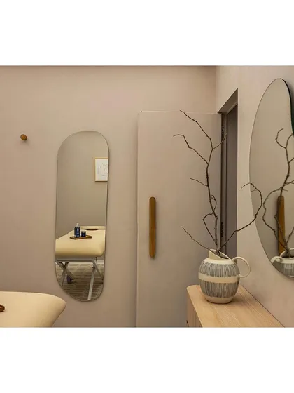 The treatment room at 'Crème' is designed as a calm, private haven. The soft, neutral palette, minimalist furniture, and organic-shaped mirrors come together to create a space that embodies the wellness brand's ethos of restrained luxury.