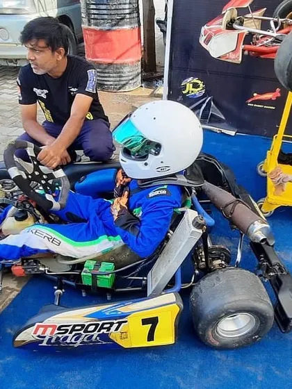 A junior driver sits in his kart, getting feedback from a team member before a session.
