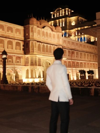 A majestic shot of our client in his white bespoke suit against the backdrop of the Jaipur City Palace at night.