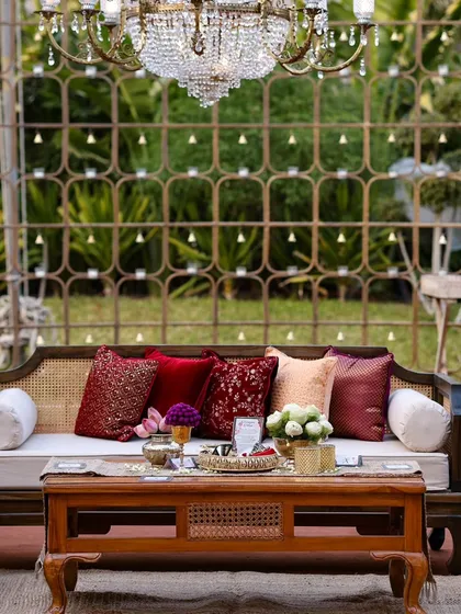 An elegant outdoor seating nook. The classic wooden sofa, rich red cushions, and a sparkling chandelier create a comfortable and luxurious space for guests to relax.
