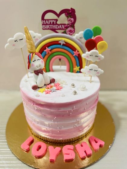 A whimsical unicorn cake sitting under a fondant rainbow and fluffy clouds. This design is perfect for a dreamy and colorful birthday party.