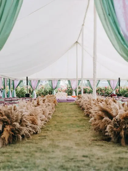The aisle for this tented wedding was lined with fluffy pampas grass, leading the eye towards the main stage. The design is earthy, natural, and completely floral-free.
