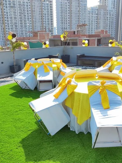 A rooftop birthday party setup with a bright yellow and white theme. We arranged round tables with chairs, all fitted with covers and sashes, and added balloon decorations for a festive look.