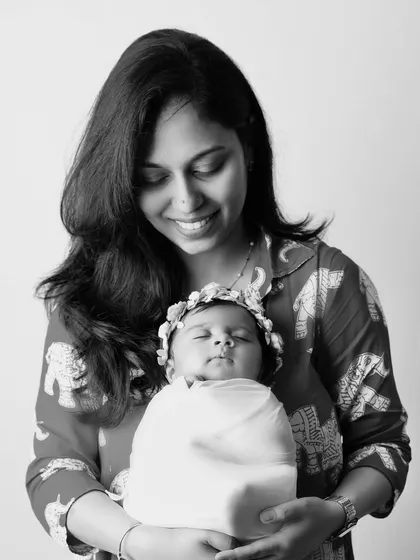 A timeless black and white portrait of a mother holding her sleeping, swaddled newborn, who is wearing a delicate floral crown.