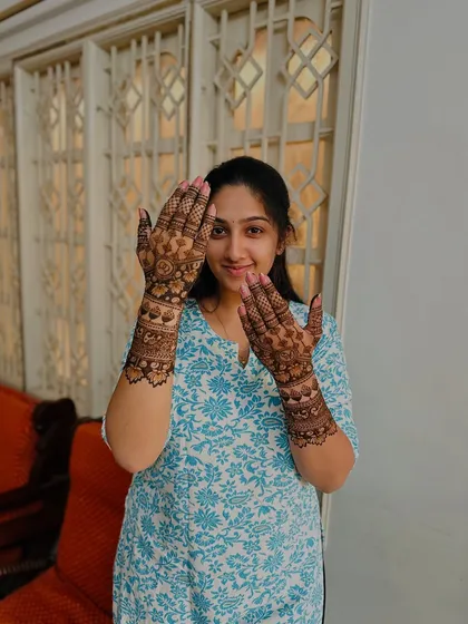 A happy client showcasing her traditional mehndi design, which features beautiful floral and geometric patterns on the hands and forearms.