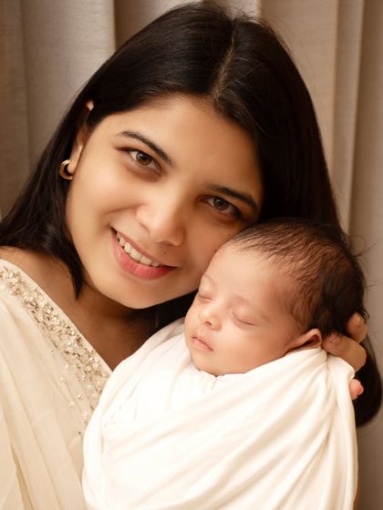 A mother's love shines through in this simple, beautiful portrait. Holding her sleeping newborn close, her gentle smile radiates warmth and happiness.